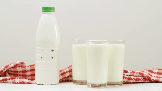 Woman puts a bottle near three glasses of fresh organic milk. Wholesome dairy and its benefits for your health