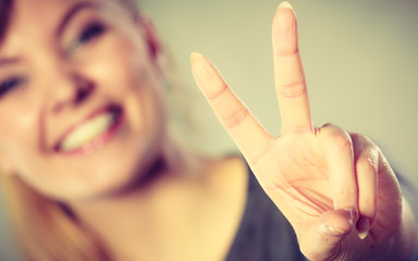Cheerful female shows victory symbol.