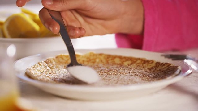 Hands of a young child sprinkling sugar and lemon juice over a thin pancake or crepe
