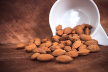 Closeup image of almonds in a white cup on wooden background