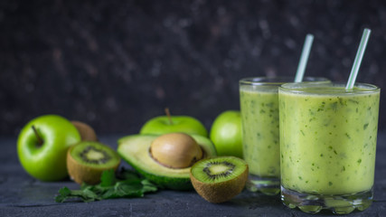 Two glass glass filled with the smoothie of avocado on wooden table with fruits. Diet vegetarian food.