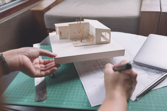 Closeup image of architects drawing shop drawing paper with architecture model on table