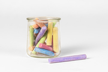 Colorful pieces of chalk in old jar on white background