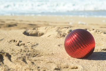 Red Christmas ball in the sand on the beach