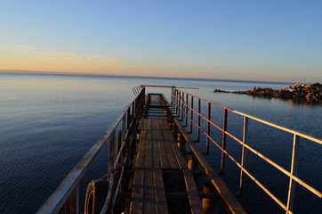 The old pier in the Volga River, lit by the sun at sunset, surrounded by water and clear sky