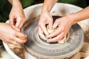Close-up of a woman potter teaches a student sculpts from a brown clay on a potter's wheel a deep cup in a workshop