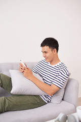 Young aisan man sitting relaxed on sofa with smartphone checking his smartphone messages