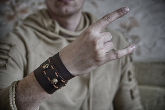 Hand with fingers folded in a "Devils horns" or "That rock's" symbol, with leather wristband and skulls on it