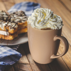 waffles with cream and chocolate on the plate and coffee on a wooden table.