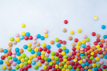 Chocolate round candy in a multicolored sugar glaze on light blue background. Selective focus. Top view. Place for text.
