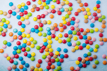 Chocolate round candy in a multicolored sugar glaze on light blue background. Selective focus. Top view. Place for text.