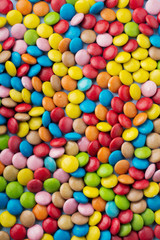 Chocolate round candy in a multicolored sugar glaze on light blue background. Selective focus. Top view. Place for text.