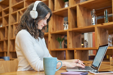 Young woman girl with long red curly hair with laptop and headphones focusing on their business passionately is typing on keyboard. Concept of blogging  in social networks and freelancing.