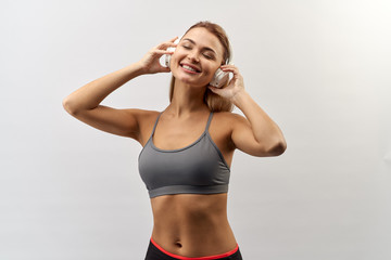 Fototapeta na wymiar joyful smiling girl in grey sport top with headphones on her head poses for a Studio portrait on a white background with a wide smile and holding hands headphones