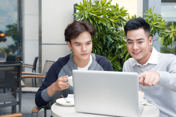 Handsome Asian business colleagues or college students work together using laptop, startup project meeting or teamwork brainstorm concept, at coffee shop or modern office