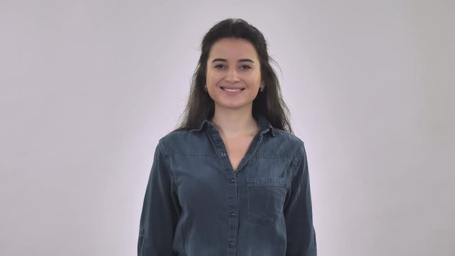 portrait attractive happy woman showing hand gesture ok. beautiful young brunette with long hair wearing in blue denim shirt posing in studio. pierce tongue