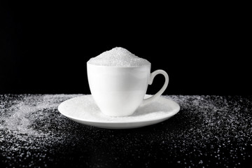 Obraz premium Pile white granulated sugar in white cup on dark background with copy space for text.