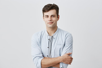 Handsome attractive young european man in casual shirt with dark hair and blue eyes, keeping arms...
