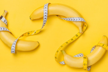 Diet, fitness and health concept presented by yellow banana wrapped in measure tape isolated on yellow paper background © makistock