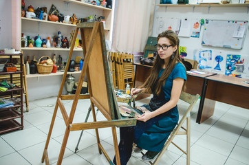 Pretty girl artist paints on canvas in art studio