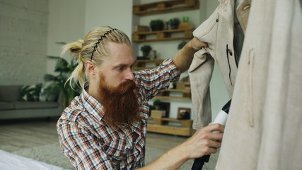 Bearded man steaming his jacket in bedroom at home