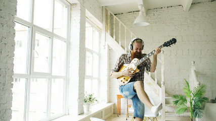 Funny bearded man dance on bed singing and playing electric guitar in bedroom at home