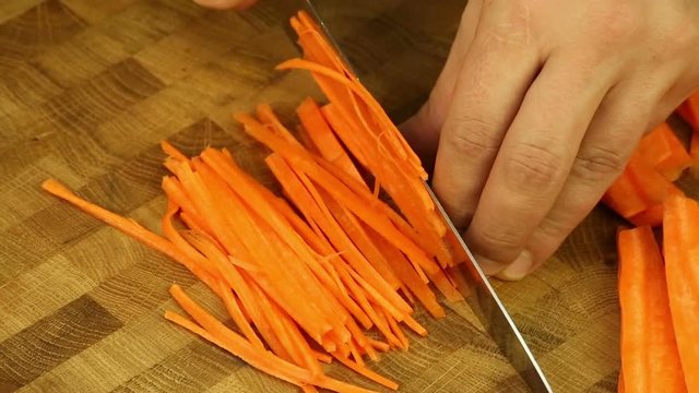 Cut carrots with a sharp knife on a wooden board