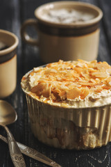 Dessert with cream sprinkled with almond petals on the wooden black table on the background of coffee cups.