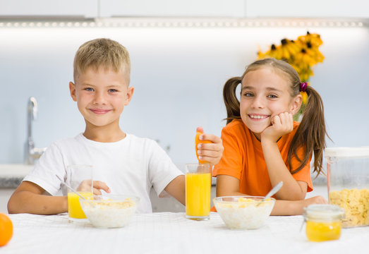 Girl and boy clink glasses with orange juice at breakfast