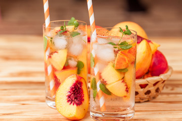 Peach lemonade with ice and mint leaves. Homemade lemonade of ripe nectarine with white and orange ripe. Two glasses of peach tea. Refreshing summer drink on a white wooden background. © Yuliia Osadcha