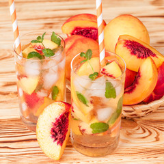 Peach lemonade with ice and mint leaves. Homemade lemonade of ripe nectarine with white and orange ripe. Two glasses of peach tea. Refreshing summer drink on a white wooden background.