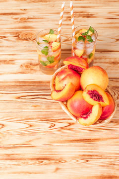 Peach lemonade with ice and mint leaves. Homemade lemonade of ripe nectarine with white and orange ripe. Two glasses of peach tea. Refreshing summer drink on a white wooden background.