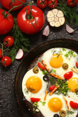Fried eggs in a cast iron pan with peppers, tomatoes, capers, herbs and bread on a black background