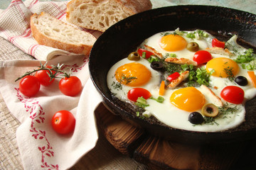 Fried eggs in a cast iron pan with peppers, tomatoes, capers, herbs and bread