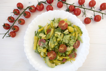 Appetizing vegetable salad consisting of tomatoes, avocado, yellow sweet pepper, lettuce and seasonings and cherry tomatoes on a branch.