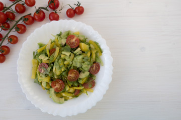 Appetizing vegetable salad consisting of tomatoes, avocado, yellow sweet pepper, lettuce and seasonings and cherry tomatoes on a branch. Space for copy space.