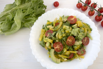 Appetizing vegetable salad consisting of tomatoes, avocado, yellow sweet pepper, lettuce and seasonings and cherry tomatoes on a branch.