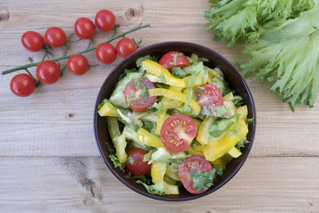 Appetizing vegetable salad consisting of tomatoes, avocado, yellow sweet pepper, lettuce and seasonings.