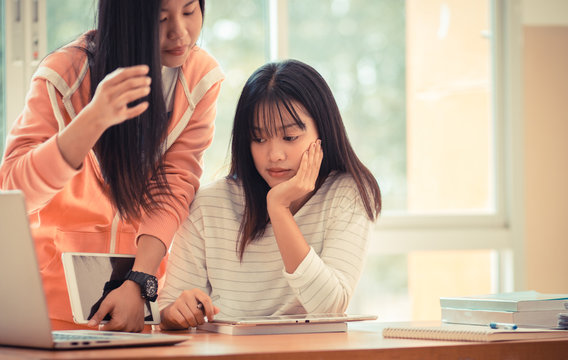 Asian University or college students studying together with tablet,laptop and documents paper for report near windows in classroom. Happy Asian young woman doing group study in Education class Concept