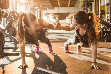 Sporty women giving high five to each other while working out together at gym.