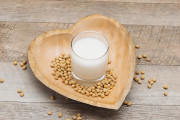 Glass with soy milk and soy bean on wooden heart shape plate
