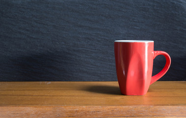 Red cup of coffee and coffee beans on the wooden table.