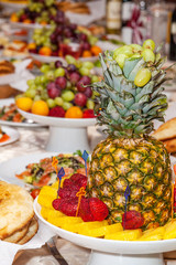 Luxuriously decorated table with tropical fruits, strawberries, bread and pineapple in the foreground