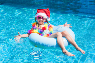 Little girl in a Santa Claus hat in a swimming pool in the tropics on holiday. The concept of a...