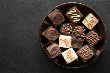 Chocolate collection in the brown plate on the dark table. Enjoying a candies. Sweets concept. Mock up for candies offers as advertising or other ideas. Empty place for a text.