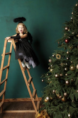 New Year's composition in the studio. A little sweet blonde in a black angel costume on the stairs...