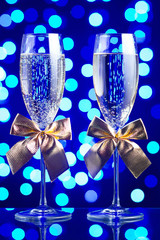 
Festive glasses with champagne and golden bows on a glass table with a beautiful blue bokeh - 184143213