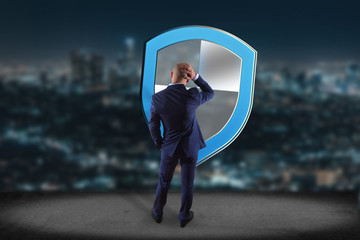 Businessman in front of a wall with a Shield symbol displayed on a futuristic interface  - Technology and security concept