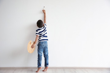 Little African-American boy painting on wall indoors