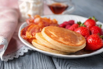 Plate with yummy pancakes, strawberry and fried bacon on wooden table